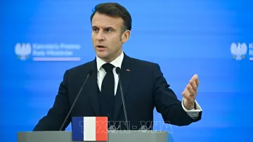 Президент Франции Эмманюэль Макрон выступает с трибуны с флагом Франции на фоне логотипа G20, комментируя подписание закона об эвтаназии