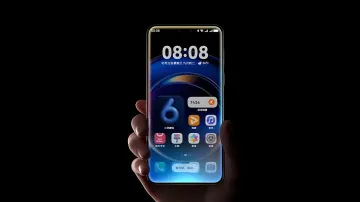 Смартфон Huawei с интерфейсом HarmonyOS 6 в руке на тёмном фоне, на экране виден виджет с цифрой 6 и фирменные иконки приложений