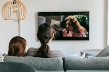 Zwei Frauen schauen einen Film auf einem Wandfernseher im Wohnzimmer — Illustration zur Meldung über den Anstieg des Film-Piraterie-Marktes in Russland