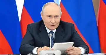 Wladimir Putin am Tisch mit Mikrofon und Dokumenten vor russischen Flaggen bei einer Sitzung, bei der er der Regierung auftrug, die Lager nach der ukrainischen Operation wiederherzustellen