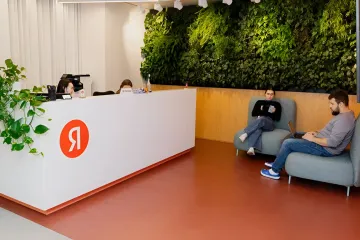 Логотип Яндекса на ресепшене офиса компании на фоне живой стены с растениями; в новостях — заполнение ИИ-поиска рекламой и доминирование Сбера и финсервисов в нейроблоке