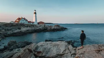 Felsige Küste von Eastport in Maine: Eine Person steht auf den Felsen am Wasser und blickt auf den Leuchtturm — diese Ufer schützen die Anwohner vor dem DeepGreen-Projekt eines Unterwasser-KI-Rechenzentrums, das ein 180-tägiges Moratorium auslöste