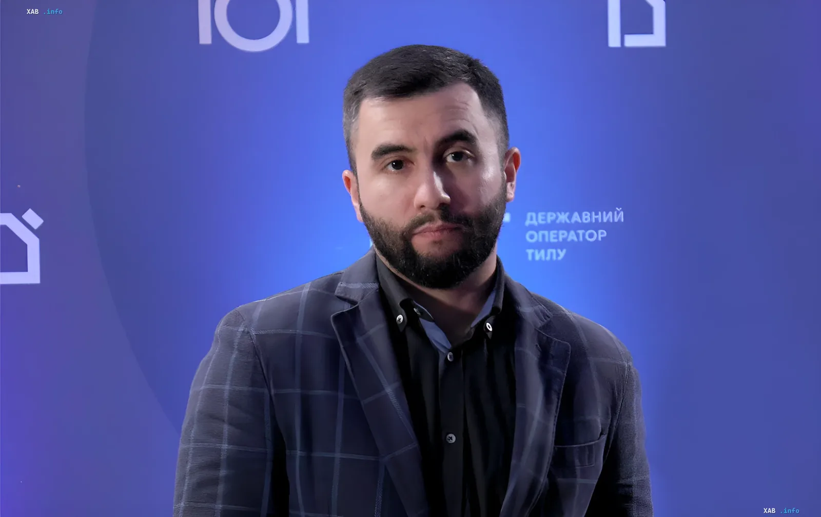 Арсен Жумадилов, отстранённый от должности главы Агентства оборонных закупок, на фоне синей стены с надписью «Державний оператор тилу»