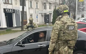 Боец ДБР в камуфляже останавливает автомобиль на фоне городской улицы во время спецоперации