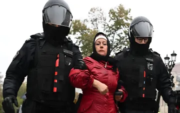 Спецназовцы в чёрной форме и шлемах сопровождают женщину в красной куртке — иллюстрация преследований, от которых BfV обещает защиту беглецам из России