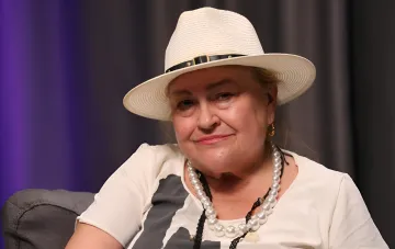 Нина Набока в светлой соломенной шляпе и жемчужном ожерелье во время интервью о бронировании артистов и отдыхе в тылу