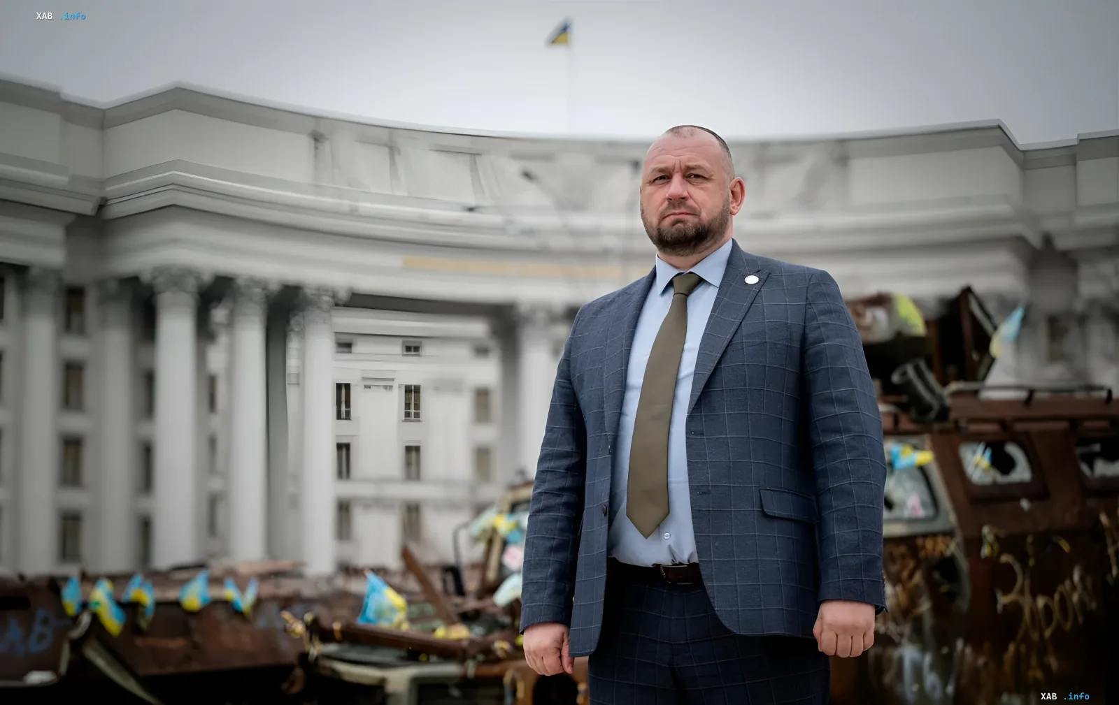 Посол Венгрии в Украине Шандор на фоне разрушенного здания и военной техники с украинскими флагами в контексте обсуждения разминирования и реабилитации военных