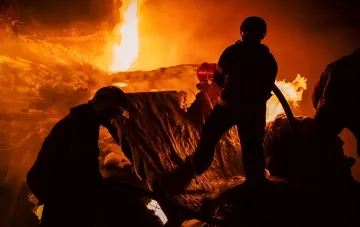 Пожарные ликвидируют последствия ночной атаки на склад в Голосеевском районе Киева: силуэты спасателей на фоне мощного огня и дыма