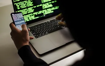 Hacker mit Laptop und Smartphone nutzt Schwachstellen in AirDrop und Quick Share für einen Remote-Angriff auf den Datei-Transfer