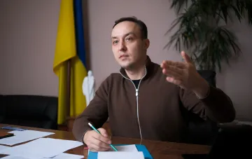 Официальный представитель Украины за столом с документами на фоне украинского флага анонсирует новые санкционные пакеты против России