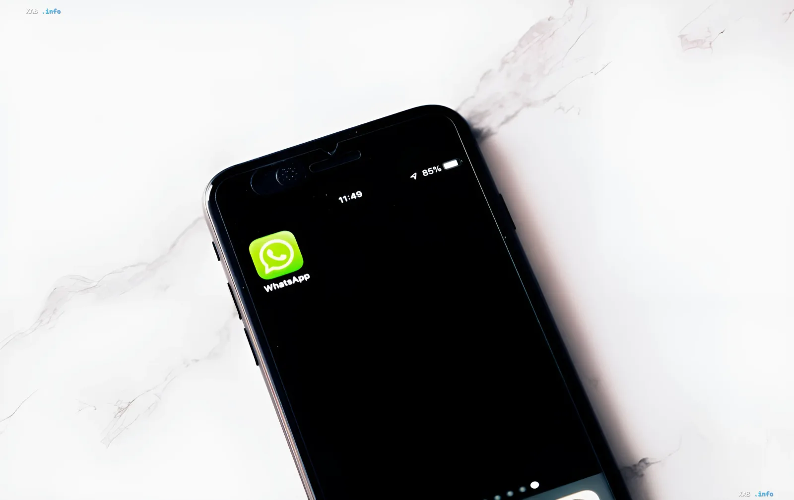 Иконка WhatsApp на экране смартфона, лежащего на мраморной поверхности, иллюстрирующая угрозы безопасности и мошеннические схемы в мессенджере