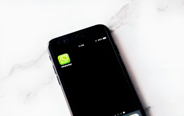 Иконка WhatsApp на экране смартфона, лежащего на мраморной поверхности, иллюстрирующая угрозы безопасности и мошеннические схемы в мессенджере