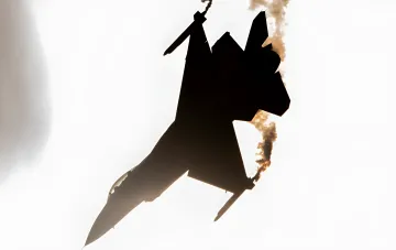 Silhouette of a J-20 stealth fighter jet against a bright sky with engine smoke — illustration for the article on AI risks in military aviation