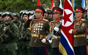 North Korean soldiers in ceremonial uniform against a backdrop of camouflaged troops — a new drone operator unit sent to Russia, total military count reaches 8,500