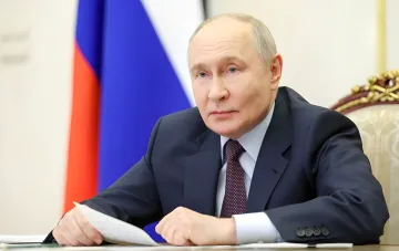 Владимир Путин за столом с документами на фоне российского флага во время обсуждения условий мирных переговоров с Украиной