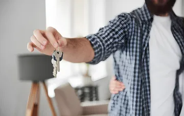 A real estate agent hands over apartment keys, illustrating the controversial double commission scheme in the rental market