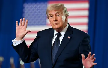 Дональд Трамп жестикулирует на фоне американского флага — новые визовые правила США оспариваются в суде