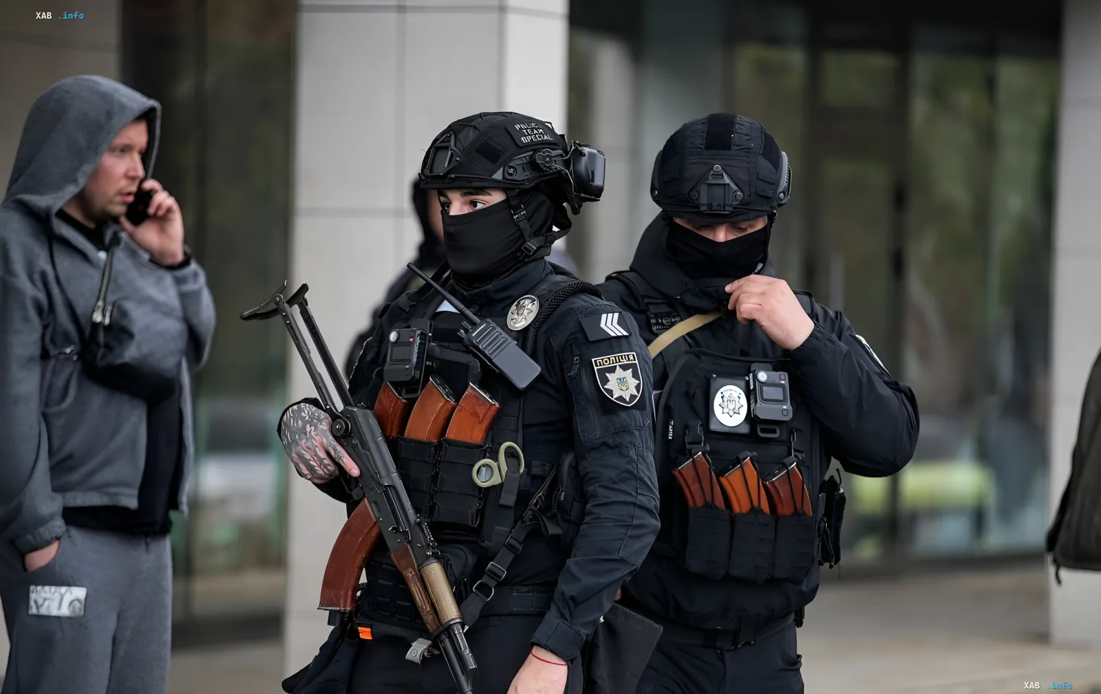 Armed police officers in tactical gear at the scene of a shooting in a supermarket near Kyiv, with a man in a hoodie talking on a phone nearby