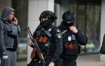 Armed police officers in tactical gear at the scene of a shooting in a supermarket near Kyiv, with a man in a hoodie talking on a phone nearby