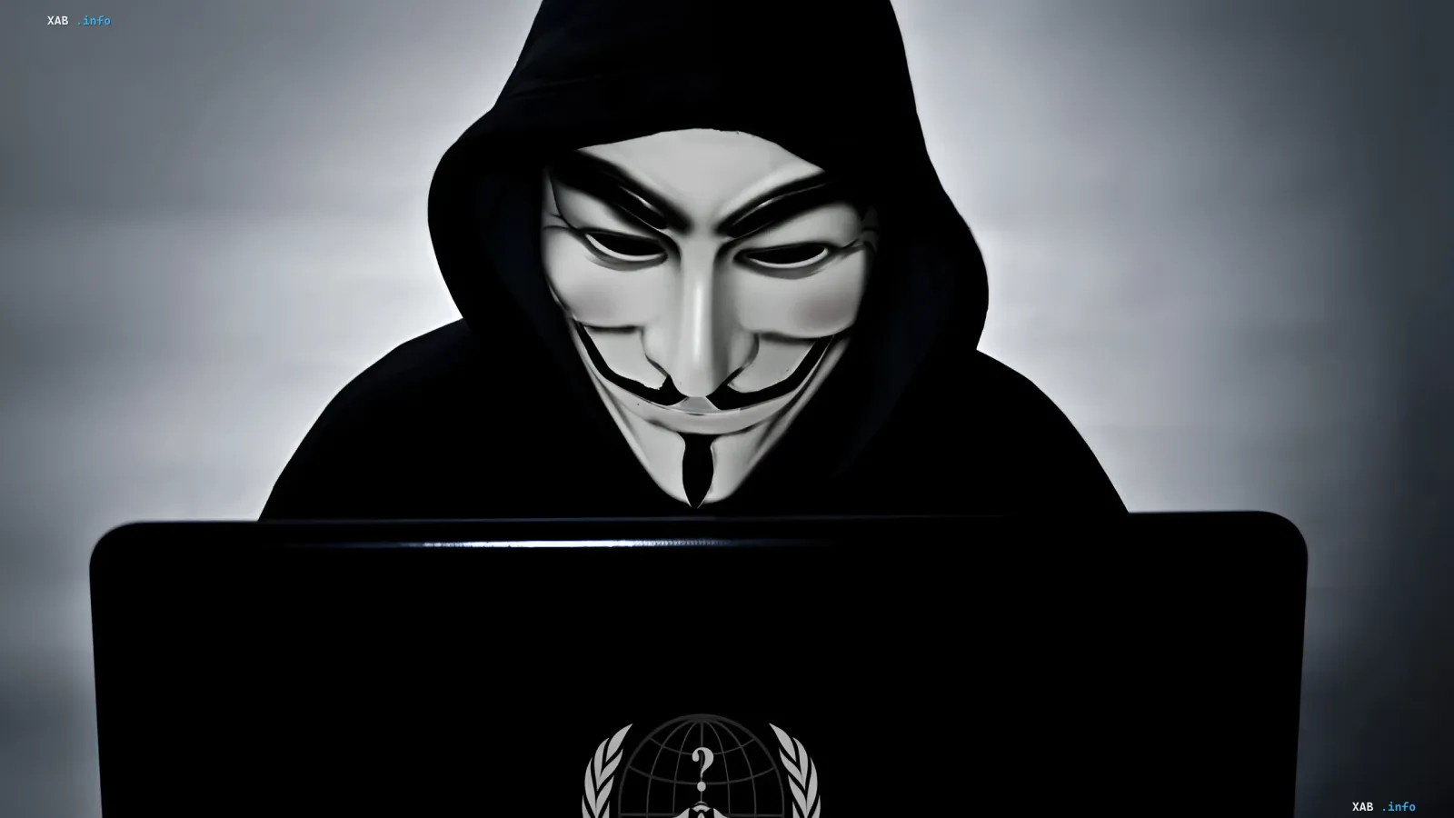Аноним в маске Гая Фокса за ноутбуком с логотипом Anonymous