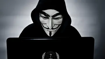 Аноним в маске Гая Фокса за ноутбуком с логотипом Anonymous