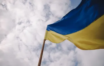 Сине-жёлтый флаг Украины на флагштоке на фоне облачного неба: происхождение и символика цветов государственного флага