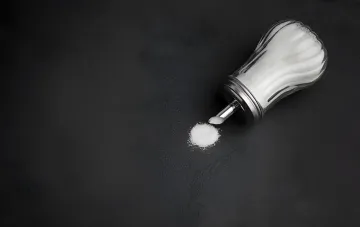 Tipped-over glass salt shaker with spilled salt on a dark background — the folk superstition about spilling salt