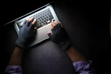 Hacker in fingerless gloves typing on a laptop in the dark, illustrating the TeamPCP supply chain attack on LiteLLM