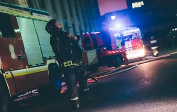 Firefighter in protective gear at the site of a drone strike on an Ozon logistics center at night