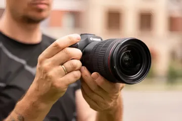 A photographer holding a professional Canon mirrorless camera with an L-series lens