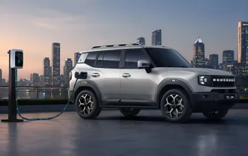 Кроссовер JETOUR T1 i-DM на зарядной станции на фоне городского небоскрёба в сумерках
