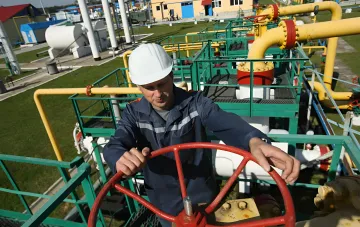 Gas field operator turning a valve handwheel against yellow pipelines — illustrating Ukraine's controlled gas export mechanism