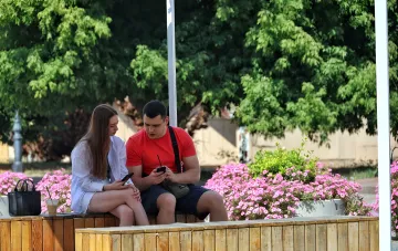Молодые люди отдыхают на солнечной парковой скамейке в Украине в тёплый августовский день без осадков при антициклоне