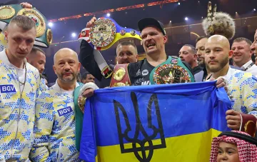 Боксёр с чемпионскими поясами WBC и WBA на фоне флага Украины с тризубом