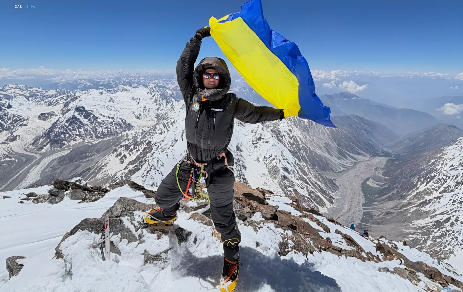 Ukrainischer Bergsteiger in funktionaler Bergausrüstung einer einheimischen Marke auf einem verschneiten Gipfel mit ukrainischer Flagge — Zeichen für den globalen Durchbruch der ukrainischen Mode