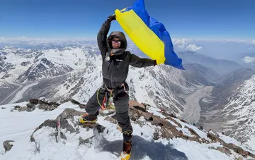 Украинский альпинист в функциональном горном костюме отечественного бренда на заснеженной вершине с украинским флагом — пример выхода украинской моды на мировую арену