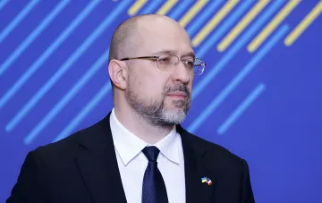 Украинский чиновник в деловом костюме с нагрудными значками флагов Украины и Франции на фоне синей панели — в контексте подготовки энергосистемы к зимним баллистическим ударам