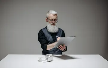 Мужчина с планшетом Apple и стилусом за столом с наушниками — иллюстрация к новости о перезапуске линейки iPad с OLED-экранами и чипами M7