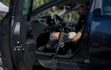 Veteran with leg amputations sits in a training car at Kyiv's municipal driving school adjusting his prosthetic before a lesson