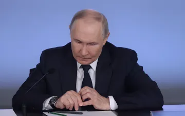 Wladimir Putin am Tisch mit Mikrofon vor dem Hintergrund absurder Rechtfertigungen des Kremls für den Einmarsch in die Ukraine