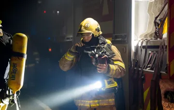 Firefighter in protective gear at night after combined attack on Ukrainian cities, preparing to deal with the aftermath