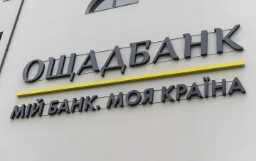 Вывеска Ощадбанка на фасаде здания на фоне новости о сбое сайта и мобильного приложения