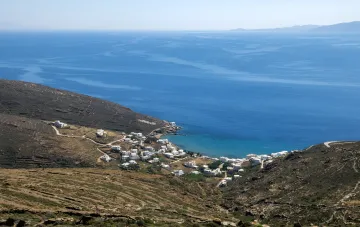 Panoramic view of Tinos: white cubic houses at the foot of a rocky hill and a turquoise bay of the Aegean Sea