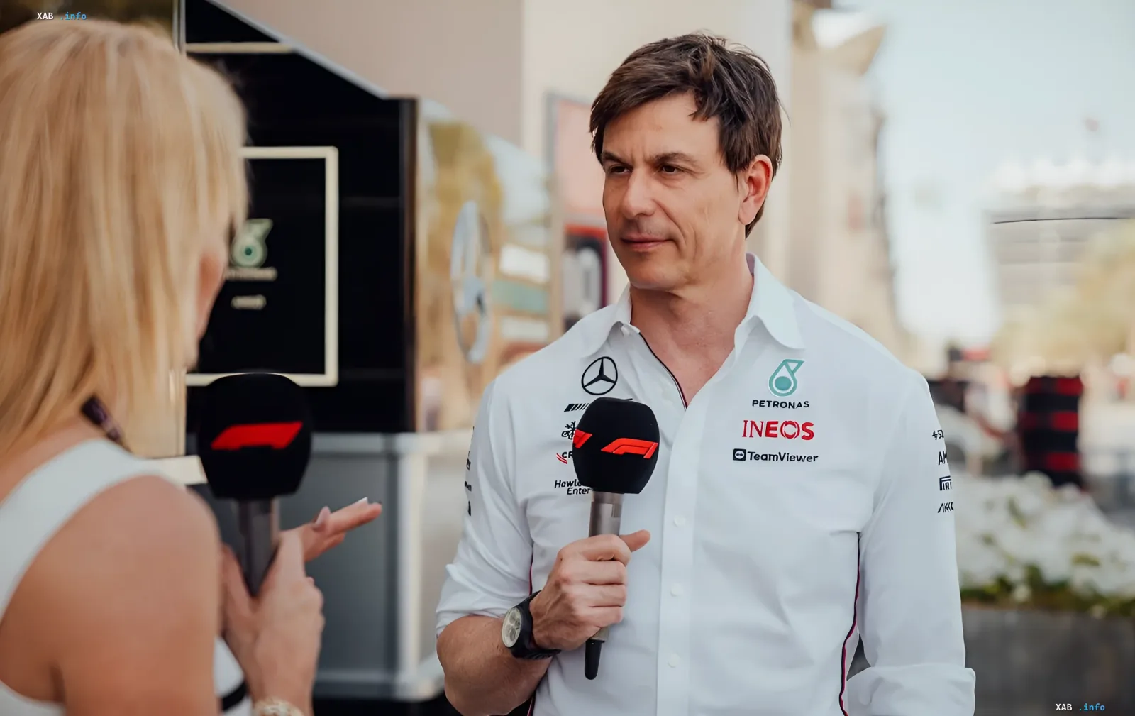 Toto Wolff in a white Mercedes-AMG Petronas F1 Team shirt with Petronas and INEOS logos holding a Formula 1 microphone during an interview