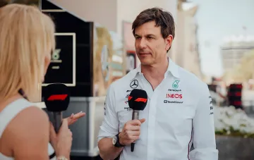Toto Wolff in a white Mercedes-AMG Petronas F1 Team shirt with Petronas and INEOS logos holding a Formula 1 microphone during an interview