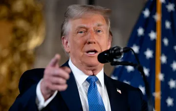 Дональд Трамп указывает пальцем во время выступления перед микрофоном на фоне американского флага — заявление о переименовании озера Онтарио в «озеро Америка»