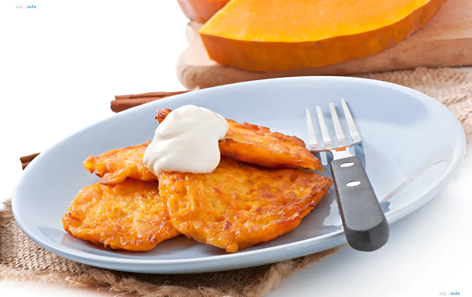 Golden pumpkin pancakes on a plate with sour cream, fresh pumpkin and cinnamon sticks — low-sugar recipe