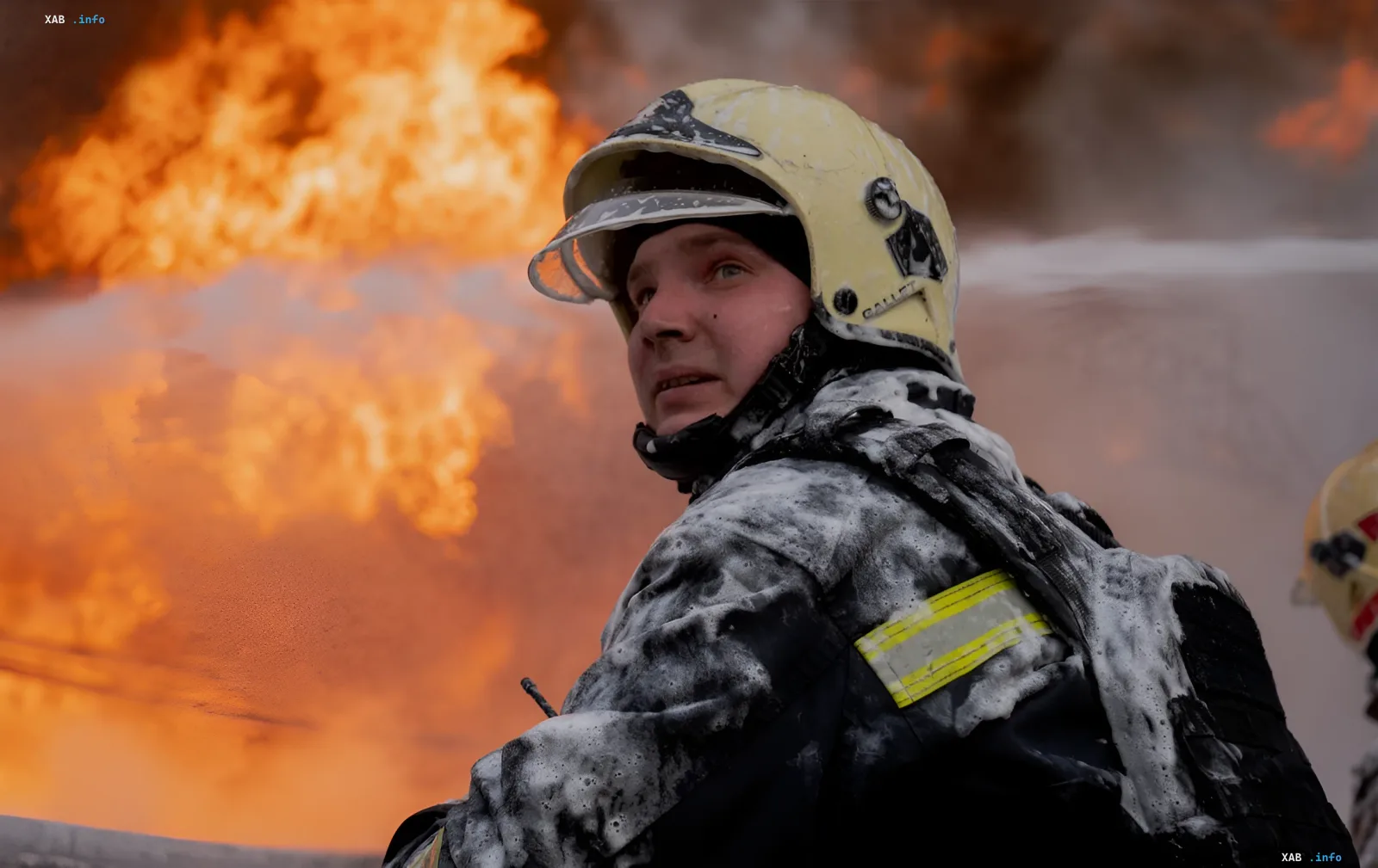 Firefighter in protective gear covered in foam against a backdrop of intense flames following a night attack on a shopping center in Dnipropetrovsk region