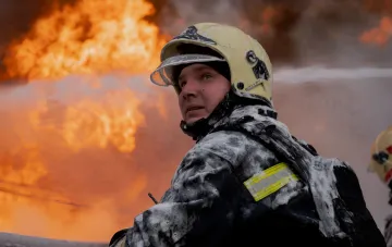 Пожарный в защитном снаряжении на фоне мощного пламени после ночного обстрела ТРЦ в Днепропетровской области