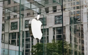Логотип Apple на стеклянном фасаде магазина на фоне новостной темы о Mac Mini на чипах M6 и M5 Pro с четырёхкратным приростом в ИИ